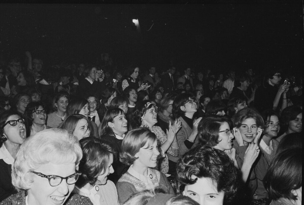 Rows of teenage fans in the Coliseum seats, many screaming and laughing