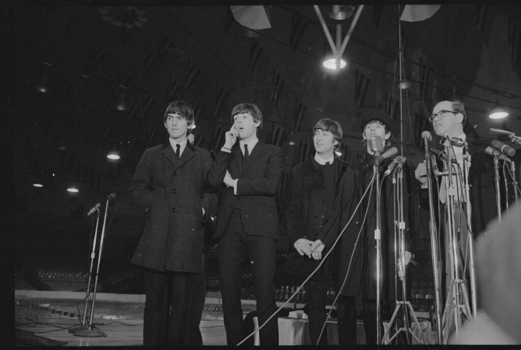 The Beatles standing behind a cluster of microphones on stands