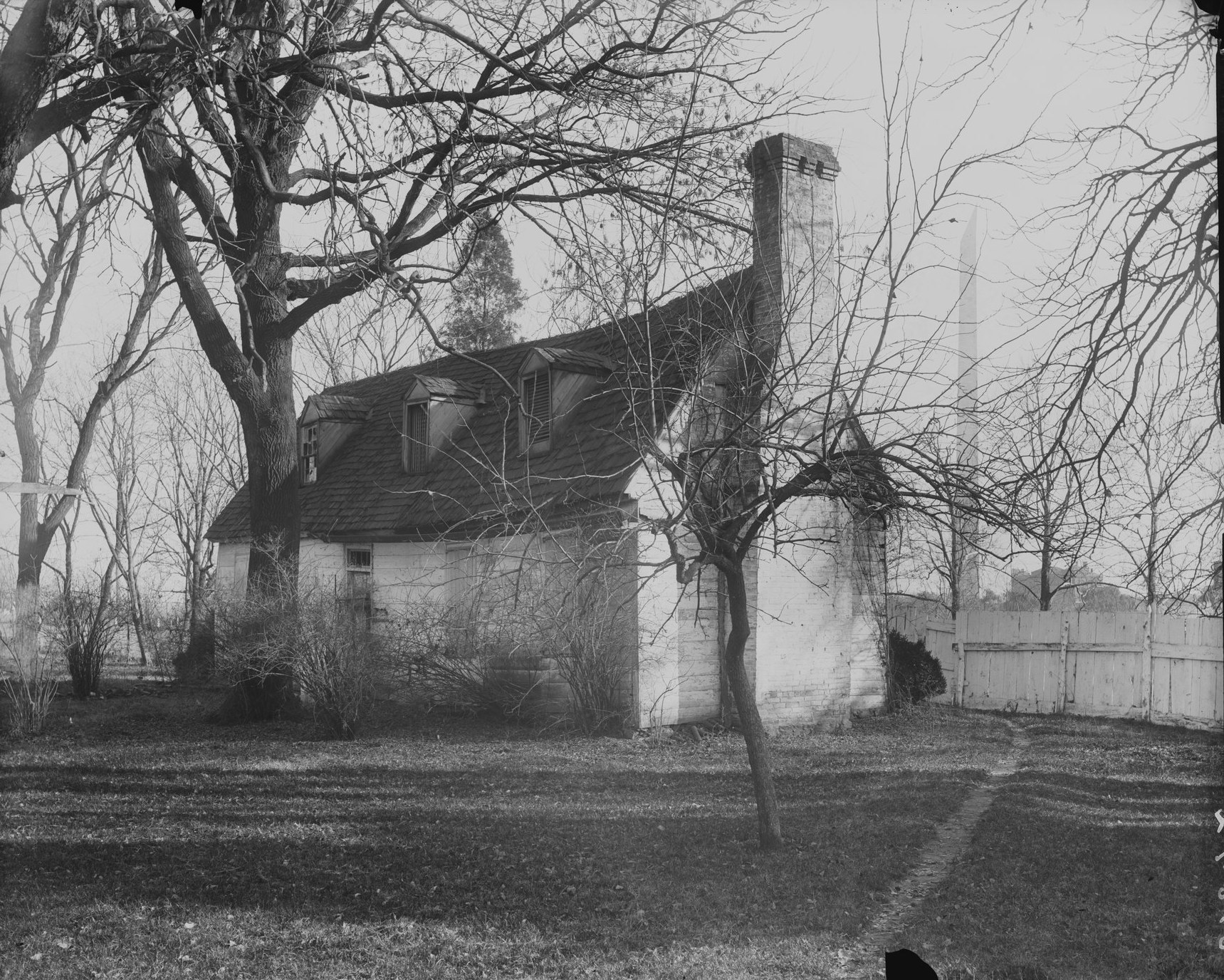 David Burnes cottage, the farmhouse of one of the original proprietors of Washington, with the Washington Monument behind it, photographed by Frances Benjamin Johnston