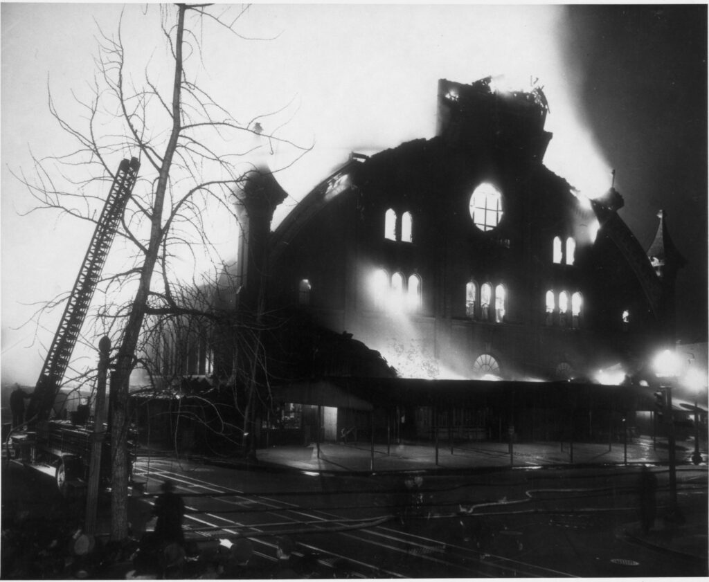 Night photograph of the Northern Liberty Market building burning on March 1, 1946, its gable end silhouetted with fire glowing through the windows and a fire ladder raised at left