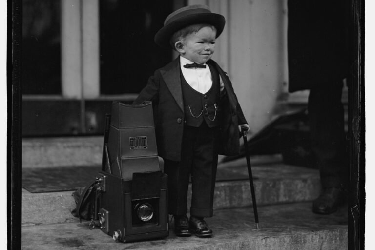 Clarence "Major Mite" Howerton in top hat and tails beside a camera