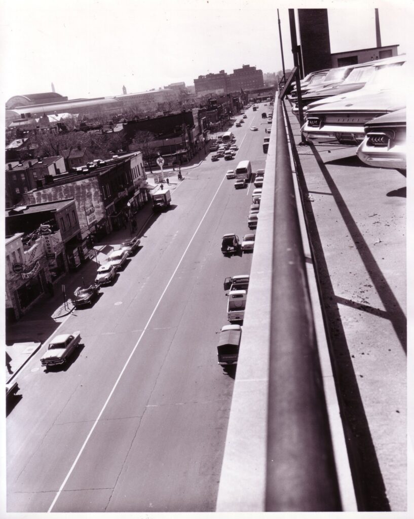 H Street NE looking west from a rooftop parking deck on April 11, 1961, with storefronts and parked cars below