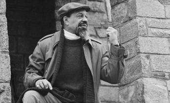 Hamaas Abdul Khaalis in a cap and coat raising a fist beside the stone wall of the Hanafi house on 16th Street NW.