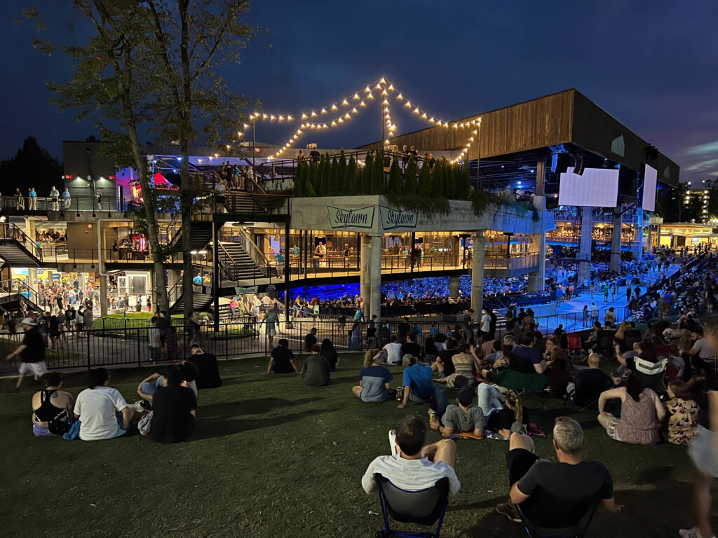 Concertgoers sit on the Merriweather lawn at night, looking toward the lit-up pavilion.