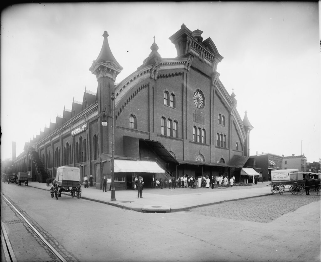 The brick Northern Liberty Market and Convention Hall at the corner of 5th and K Streets NW around 1920, with corner turret, rose window, awnings and wagons at the curb
