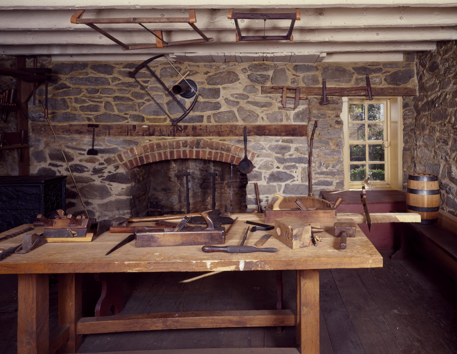 Restored interior room with exposed fieldstone walls, a large hearth and a wooden workbench covered with hand tools