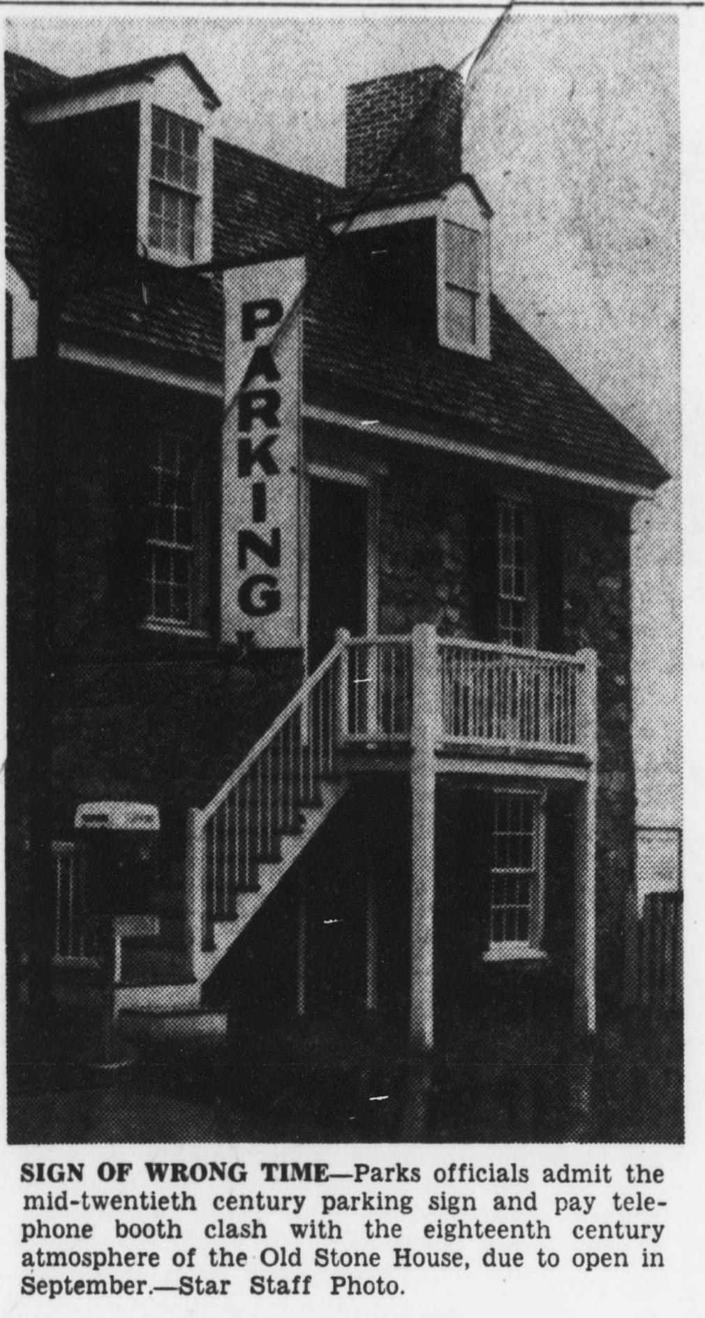 Newspaper photo of the Old Stone House with a large vertical PARKING sign mounted on its front and a pay phone booth beside the stairs