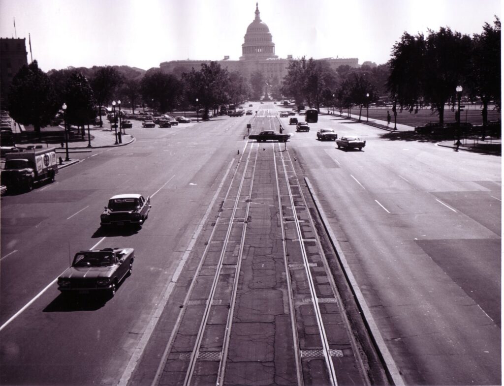 Abandoned streetcar tracks down the center of Pennsylvania Avenue NW leading to the U.S. Capitol in 1962, with a convertible and sedans driving alongside